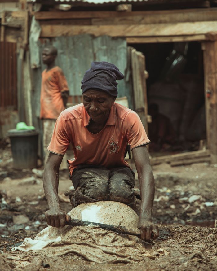 A man kneeling and working on a dusty urban street with makeshift structures.