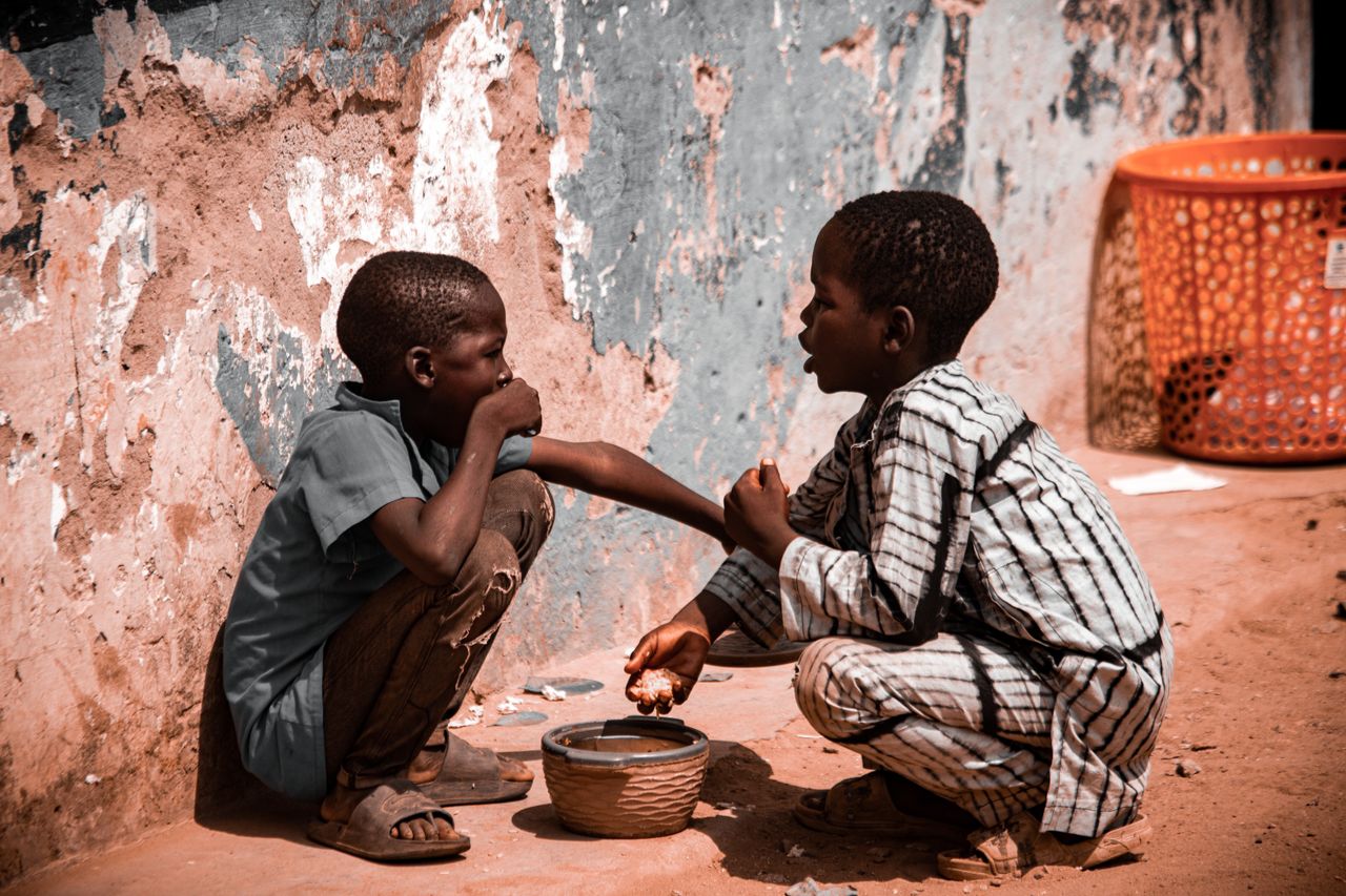 services-04 Two children sharing food, depicting childhood and poverty in a rural outdoor setting.
